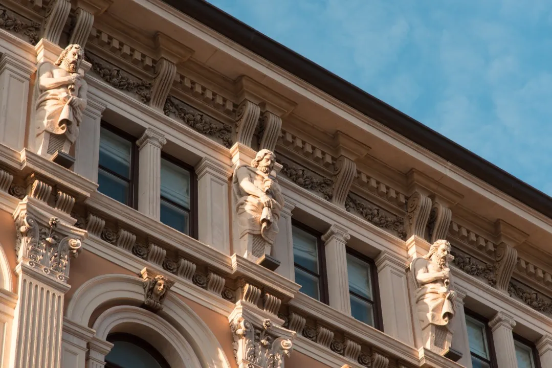 Fotografía de una fachada arquitectónica color beige con acabados detallados como figuras y columnas.