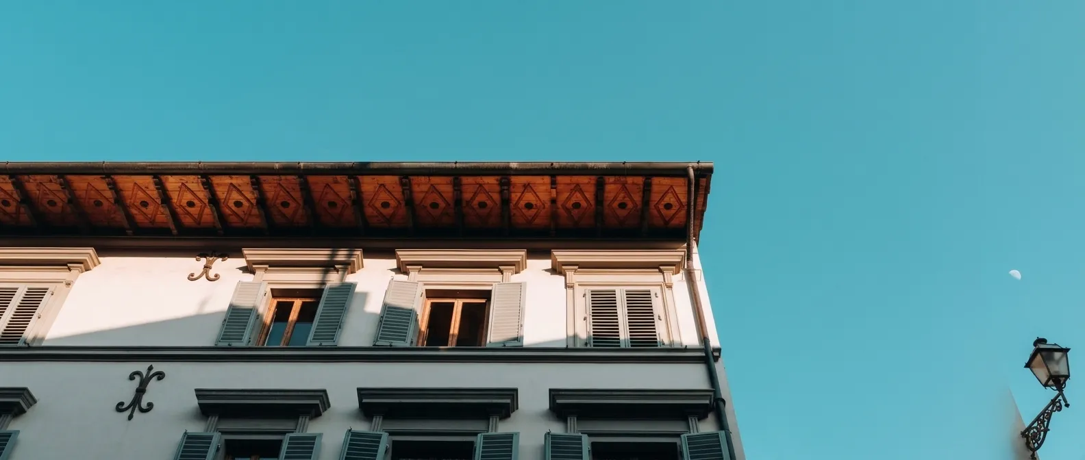 Fotografía desde abajo de una fachada arquitectónica color blanco con beige techo sobresaliente color café.